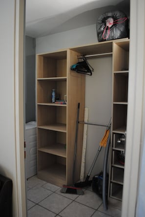 Un placard de rangement avec plusieurs étagères, un aspirateur et un balai.
