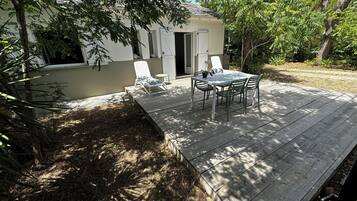 A wooden deck with a table and chairs, surrounded by trees and a building with a door.