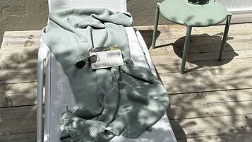 Una silla lounge blanca con una manta verde y gafas de sol, sobre una terraza de madera.