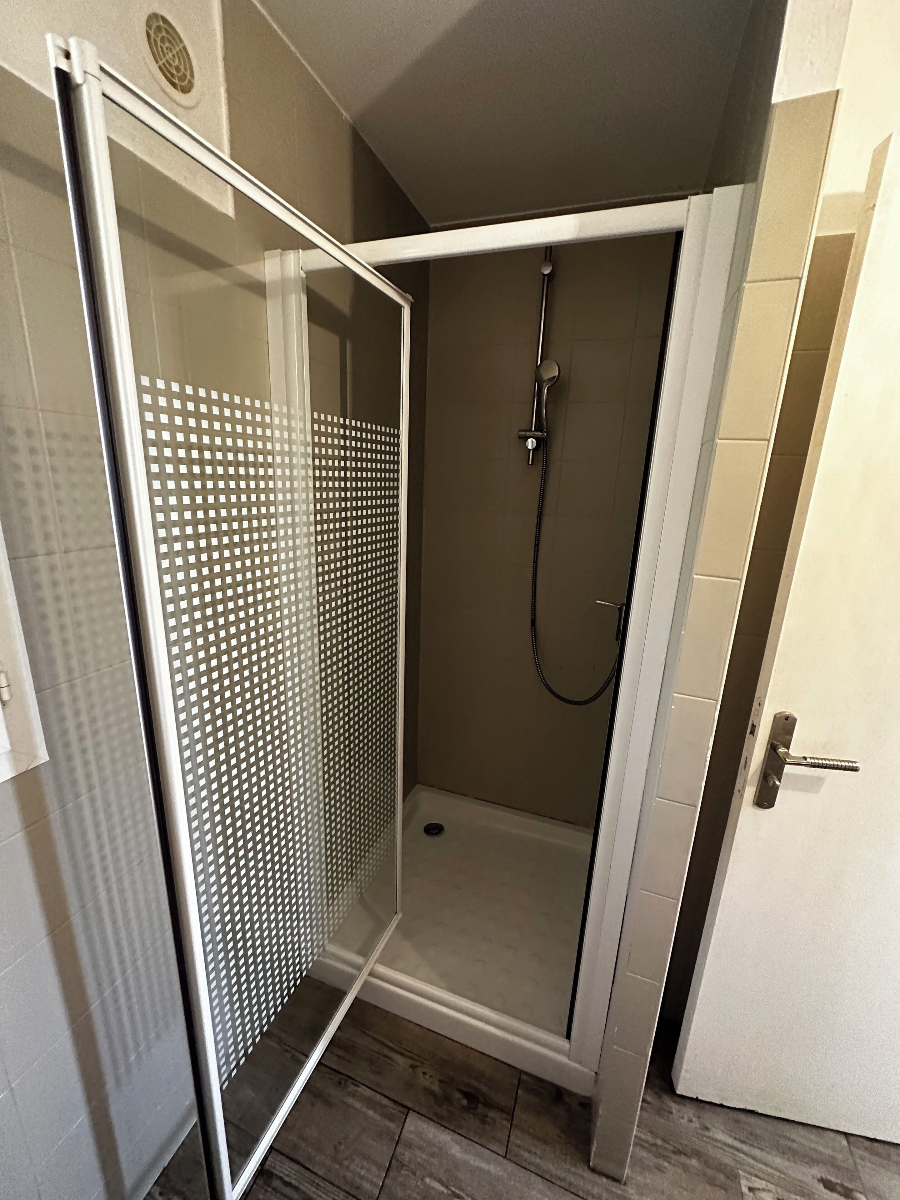 Un petit espace douche fermé, doté d’une porte en verre et d’un pommeau de douche.