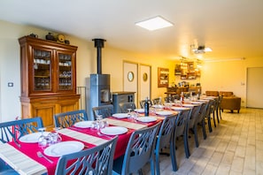 Ein Essbereich mit einem langen Tisch, der für eine Mahlzeit gedeckt ist, einem Kaminofen und einer Bar im Hintergrund.