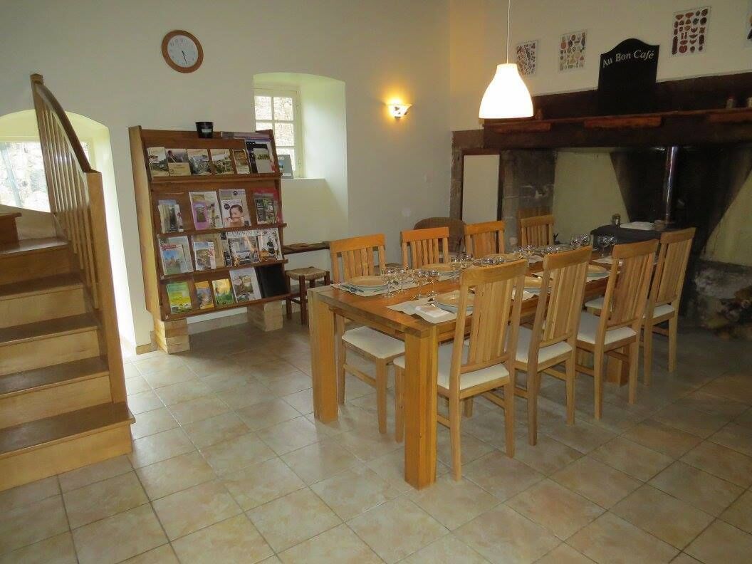A dining area with a wooden table and chairs, a bookshelf, a clock, and a sign reading "Au Bon Cafe".