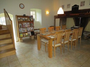 Un coin repas avec une table et des chaises en bois, une bibliothèque, une horloge et une enseigne indiquant « Au Bon Café ».