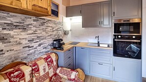A compact kitchen with grey cabinets, a stone backsplash, and a wooden ceiling.