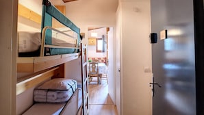 A compact room with bunk beds, a wooden ceiling, a door, and a small kitchenette area.