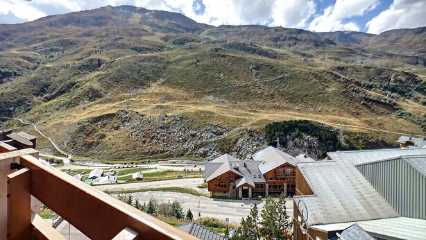 A mountain lodge with a large building and a parking area in the foreground, surrounded by hills and a clear sky.