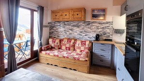 A cozy room with a wooden sofa, a kitchen with modern appliances, and a view of the outdoors.