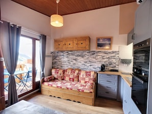Um quarto aconchegante com um sofá de madeira, cozinha equipada com eletrodomésticos modernos e vista para o exterior.