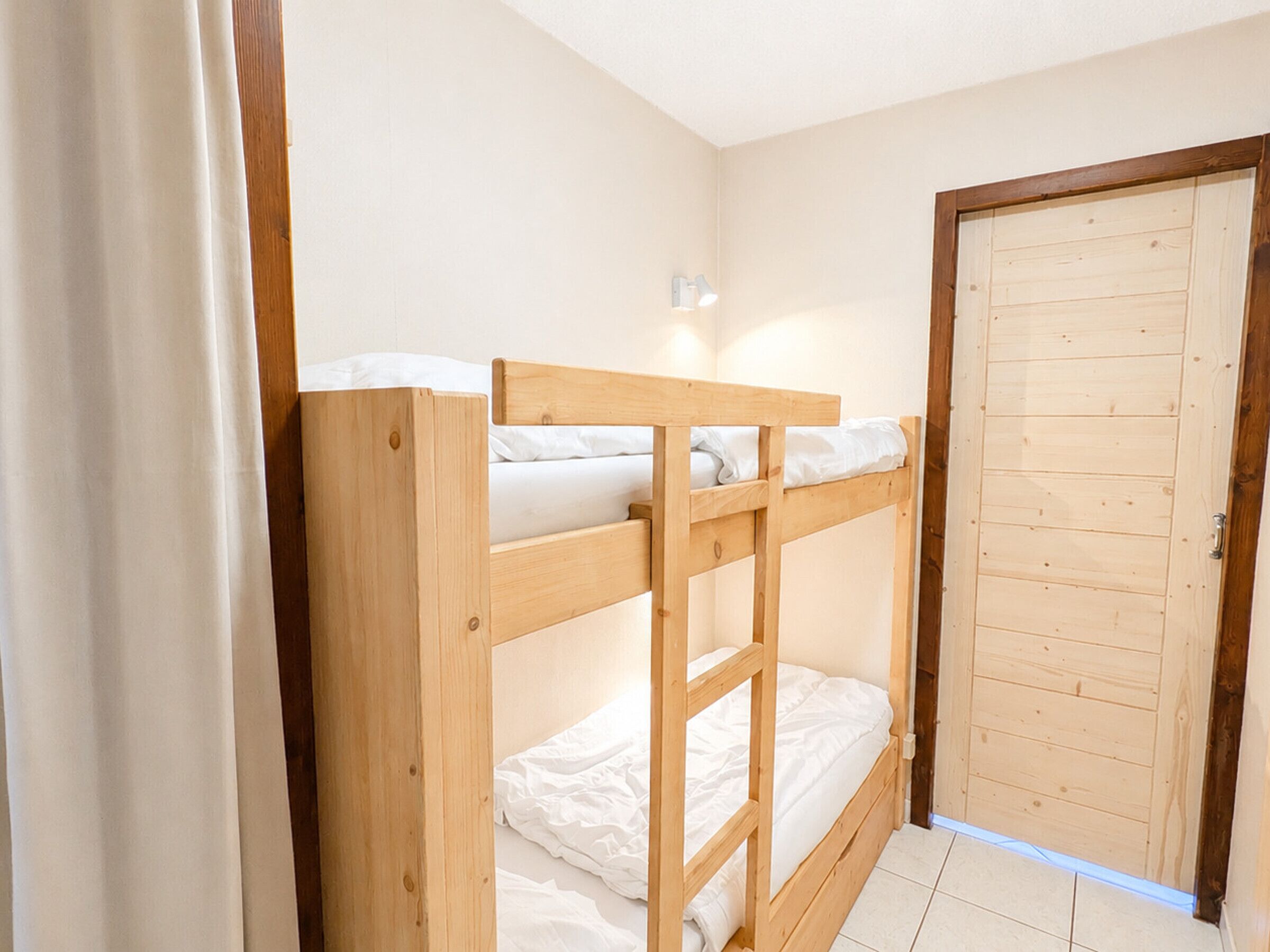 Een slaapkamer met een stapelbed, een houten deur en een gordijn.