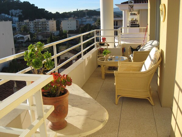 A balcony with wicker furniture, a potted plant, and a view of the cityscape.