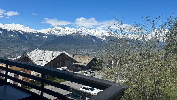 A mountain view with snow-capped peaks, a town below, and a balcony with a view.