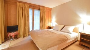 A hotel room with a large bed, a television on a small table, and curtains on the windows.