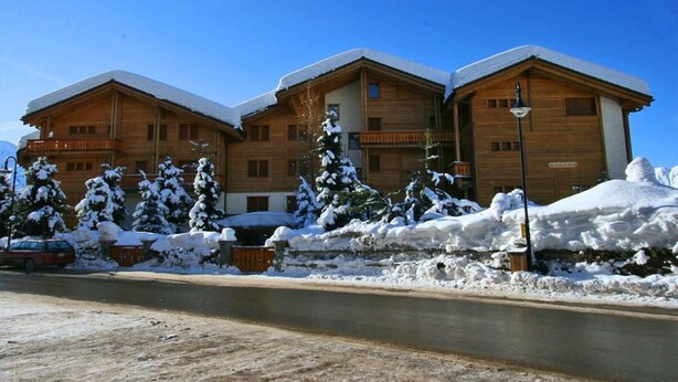 A wooden building with multiple balconies and snow-covered trees.
