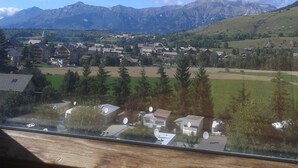 Udsigt over en bjergby med huse og kirke, omgivet af grønne marker og bjerge.