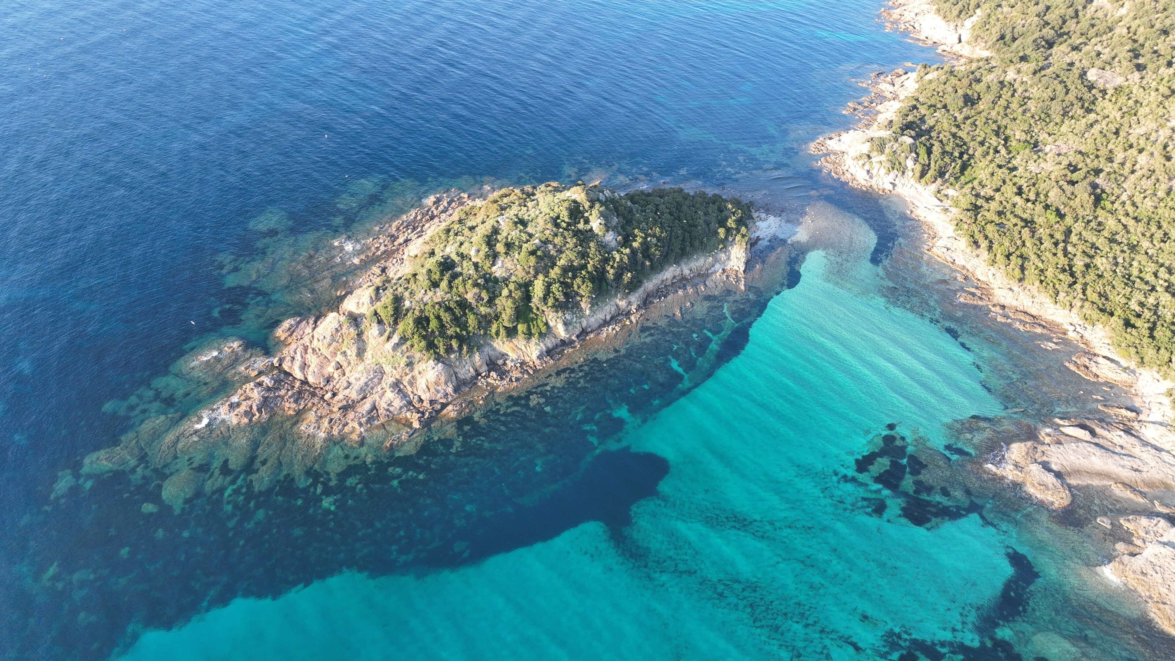 Luchtbeeld van een kusteiland met helder turquoise water en rotsachtig terrein.