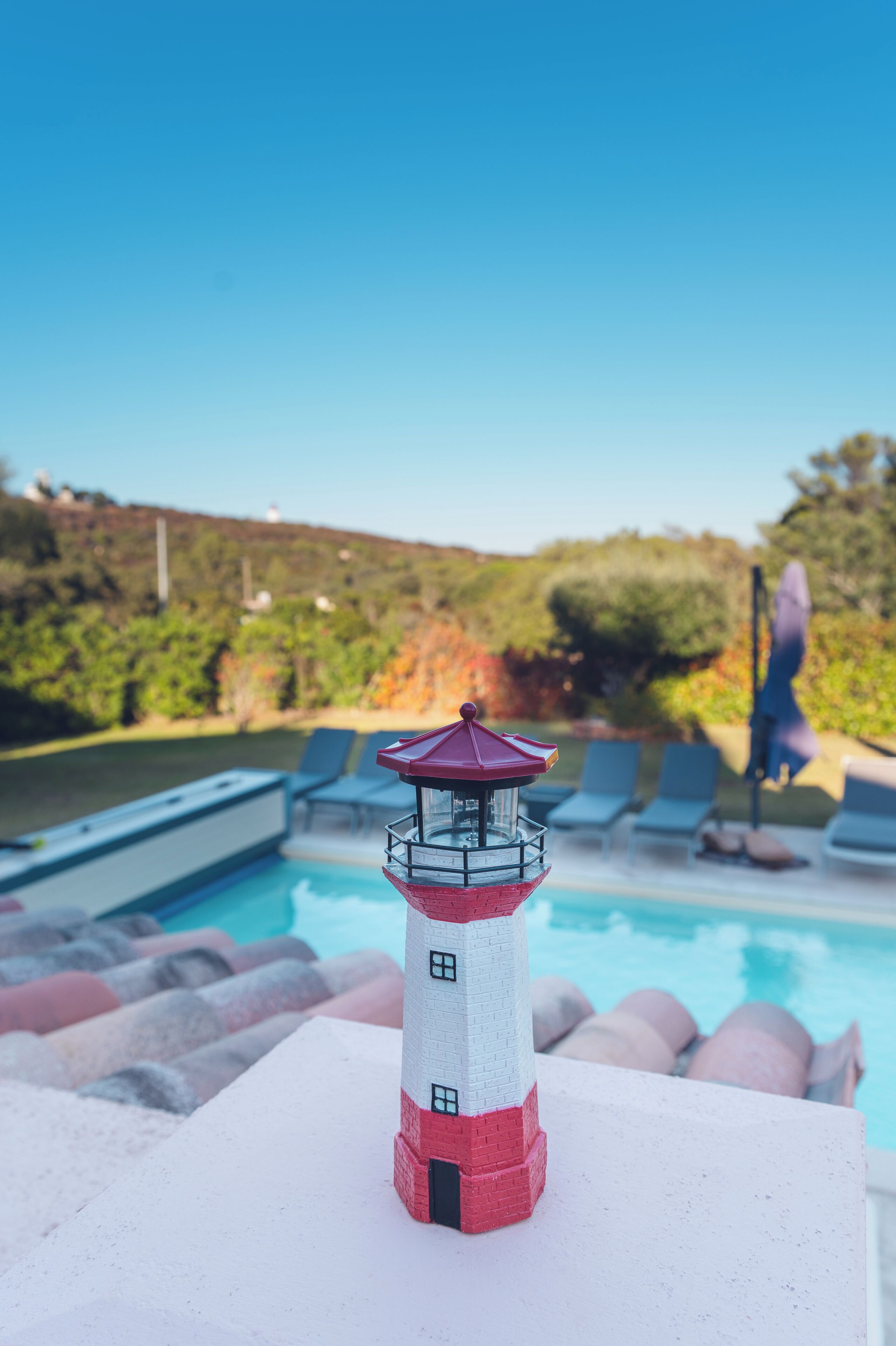 A small lighthouse model near a pool with lounge chairs and a clear sky.
