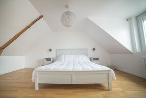 A bedroom with a sloped ceiling, a bed with white bedding, two bedside tables with lamps, and a large window on the right. - Holiday house 6 pers. in Etel, beach at 100 m (Étel)