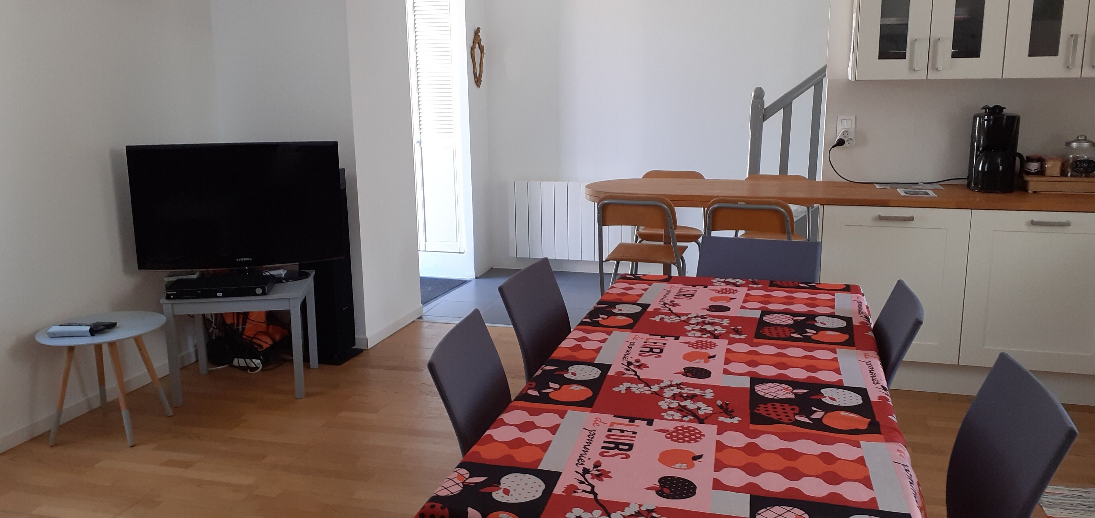 Un espace de vie compact comprenant une table à manger, des chaises, un téléviseur et une petite cuisine.