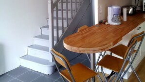 A kitchen with a wooden table, two chairs, a coffee maker, and a toaster. - Holiday house 6 pers. in Etel, beach at 100 m (Étel)
