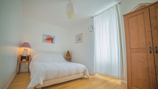 A bedroom with a bed, a nightstand, a lamp, a wardrobe, and two framed pictures on the wall. - Holiday house 6 pers. in Etel, beach at 100 m (Étel)