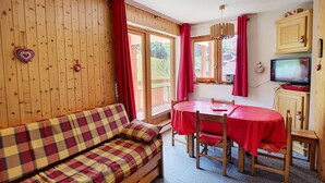 Ein gemütliches Zimmer mit einem Karomuster-Sofa, einem Esstisch mit Stühlen, einem Fernseher und einer Holzwand mit Herzdekorationen.