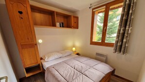 Une chambre à coucher avec un lit, des étagères en bois, une table de chevet, une fenêtre avec des rideaux et un radiateur.