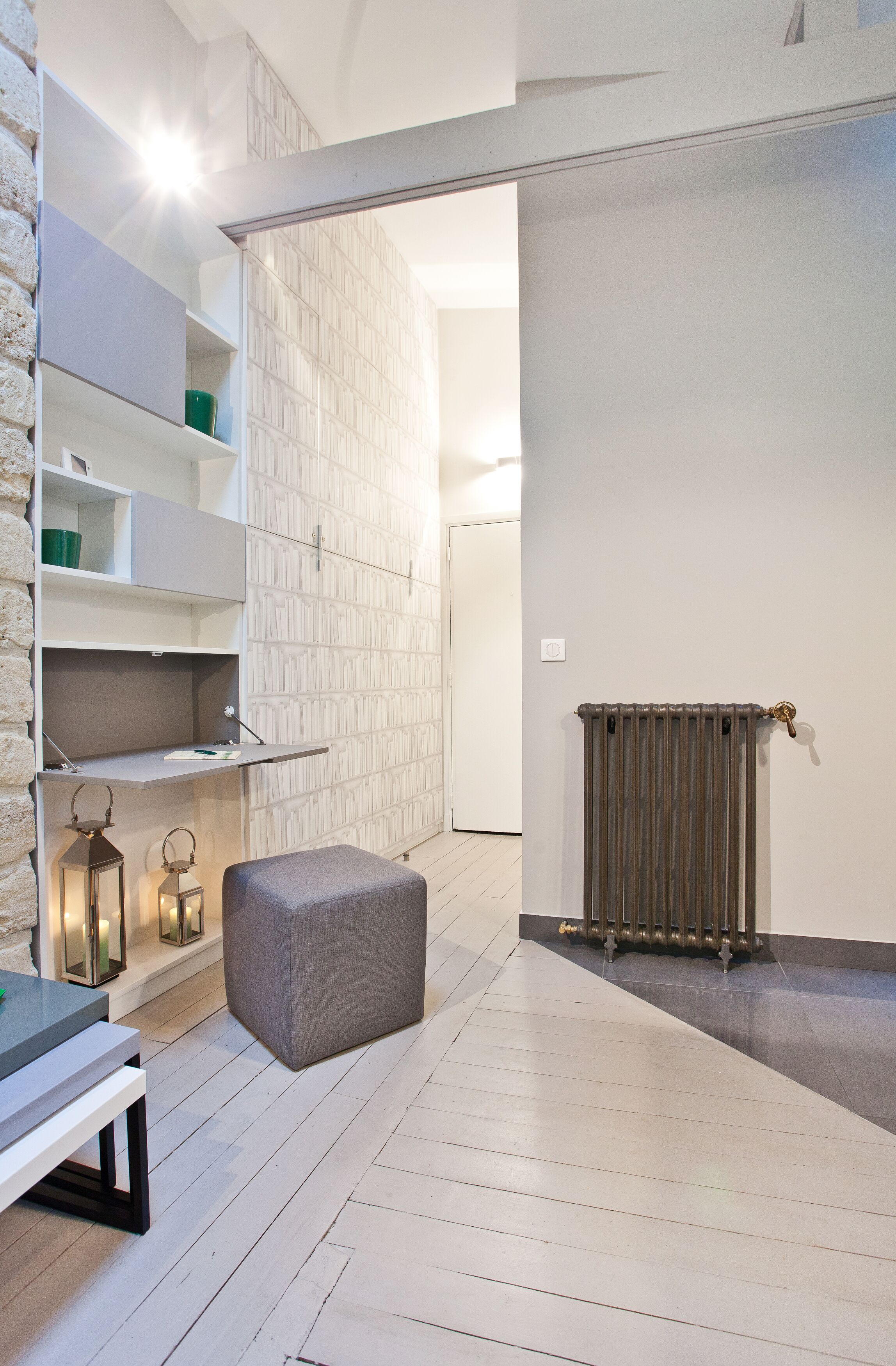 Habitación moderna y minimalista con paredes blancas, suelo de madera, un radiador y una banca gris.
