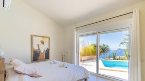 A bedroom with a large bed, a painting on the wall, and a view of a pool and landscape through a sliding door. - Altea HILLS, Luxury Villa, Wonderful View! (Altea)