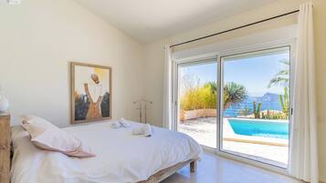 Un dormitorio con una cama grande, un cuadro en la pared y vistas a una piscina y paisaje a través de una puerta corrediza.