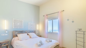 A neatly made bed with pillows and rolled towels, a bedside table, a wall-mounted light fixture, and a window with curtains. - Altea HILLS, Luxury Villa, Wonderful View! (Altea)