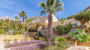 A modern building with a stone retaining wall, palm trees, and a variety of desert plants. - Altea HILLS, Luxury Villa, Wonderful View! (Altea)