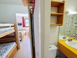 Une chambre avec des lits superposés, une salle de bain avec un lavabo jaune et un mur carrelé.