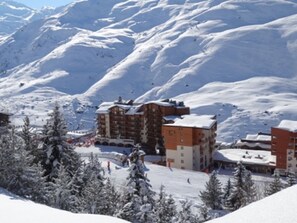 Una località montana innevata con edifici a più piani, piste da sci e alberi coperti di neve.