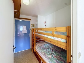 Une pièce avec un lit superposé, une porte bleue et une petite étagère sur laquelle se trouve un objet rouge.