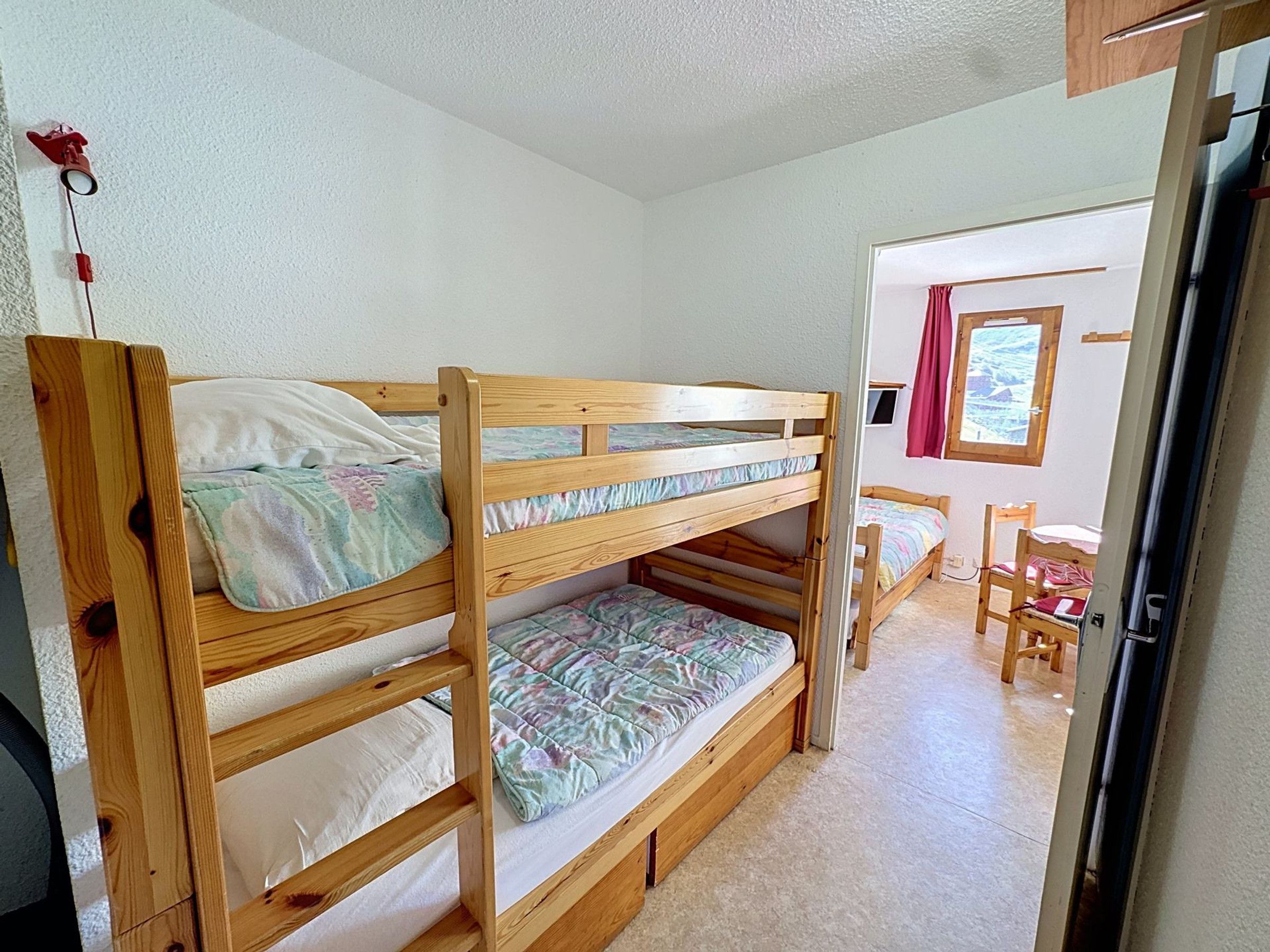 Una cama litera con estructura de madera, una ventana con vistas y una puerta que da a otra habitación.