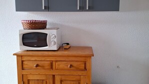 Un microondas sobre un mueble de madera con cajones, una cesta encima y un armario gris arriba.