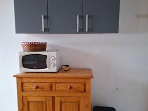 Un forno a microonde su un mobiletto in legno con cassetti, un cesto sopra e un armadietto grigio sopra.