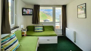 Ett litet hotellrum med ett enda rum, med en grön säng, en tv på väggen och ett fönster med utsikt över ett kuperat landskap.