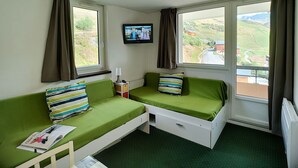 Ett rum med två gröna sängar, en tv och ett fönster med utsikt över en dal.