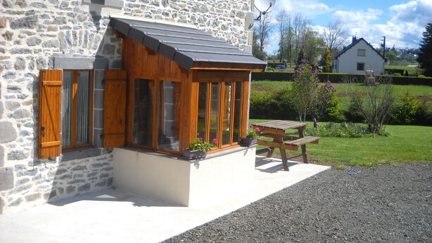 A stone house with a wooden porch, a satellite dish, and a gravel driveway.
