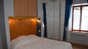 A bedroom with a wooden headboard, a bed with white bedding, a window with blue curtains, and a radiator below the window.
