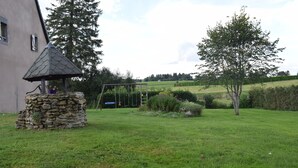 A stone structure with a small roof, a swing set, and a tree in a grassy area.