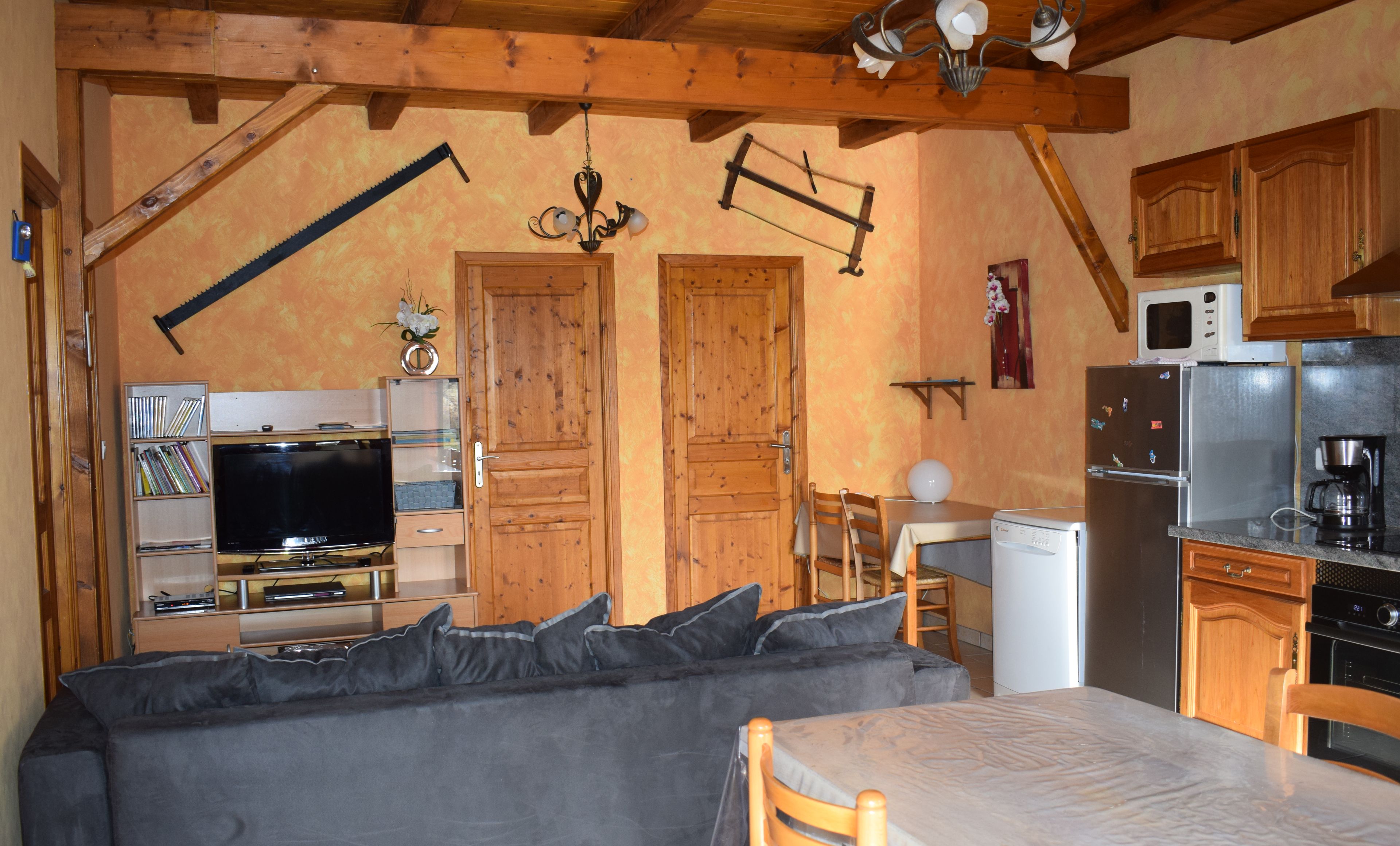 A cozy room with a bed, a TV, a small kitchen, wooden cabinets, and a dining table.