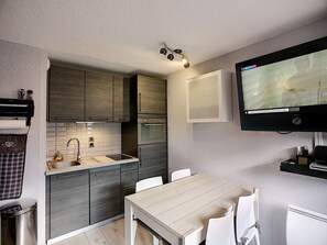 A modern kitchen with dark wood cabinets, a built-in oven, a sink, and a dining area with a white table and chairs. - Renovated 2-room apt 4 pers, slopeside, southwest (Les Menuires)