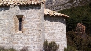 A stone building with a tiled roof, a small window, and a mountainous backdrop.