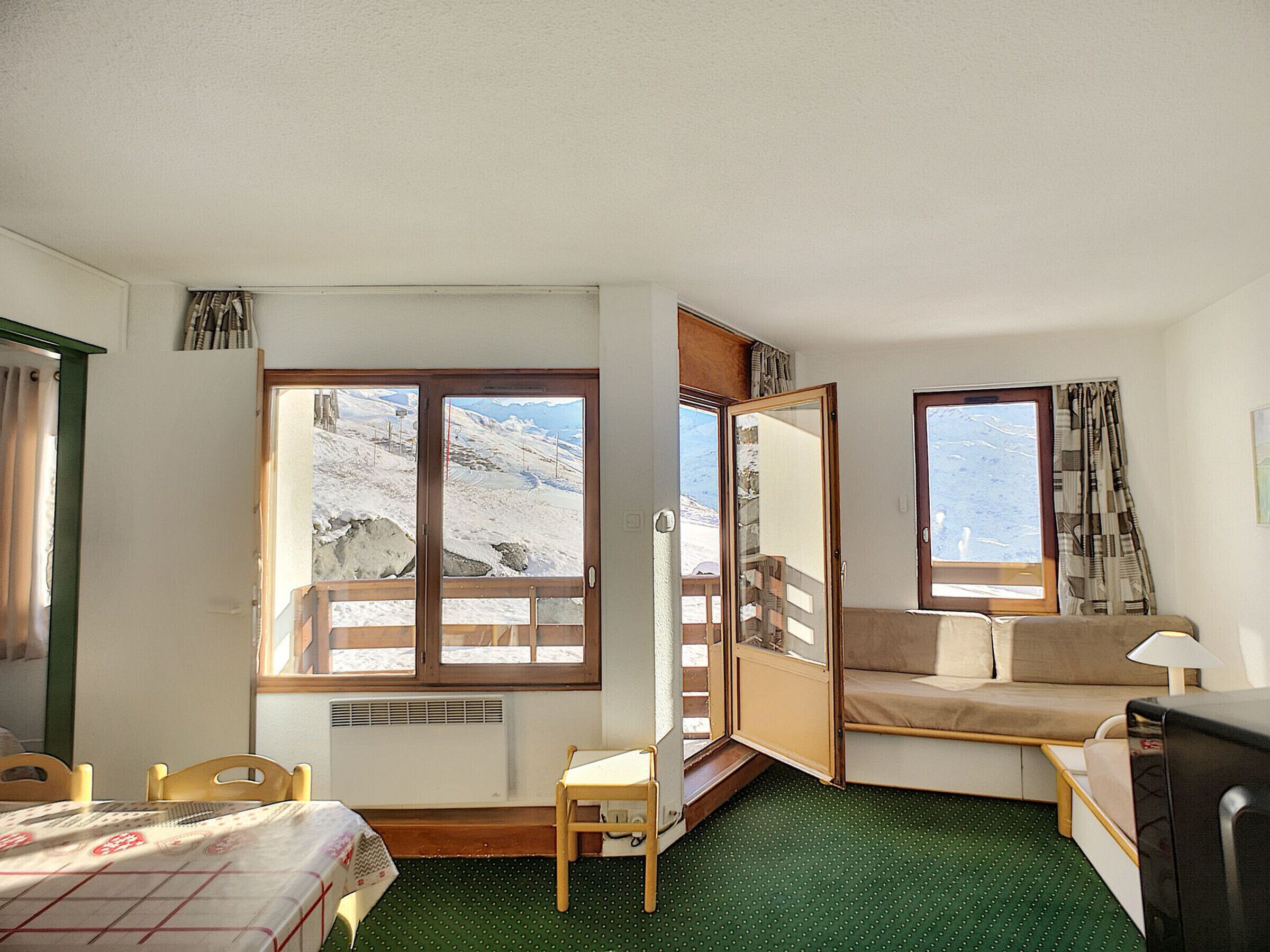 A hotel room with a bed, a small table, a chair, a sofa, and a window with a view of a snowy landscape.