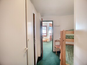 Cozy room with a bunk bed, featuring a door and a window, carpeted floor, and a wooden chair.