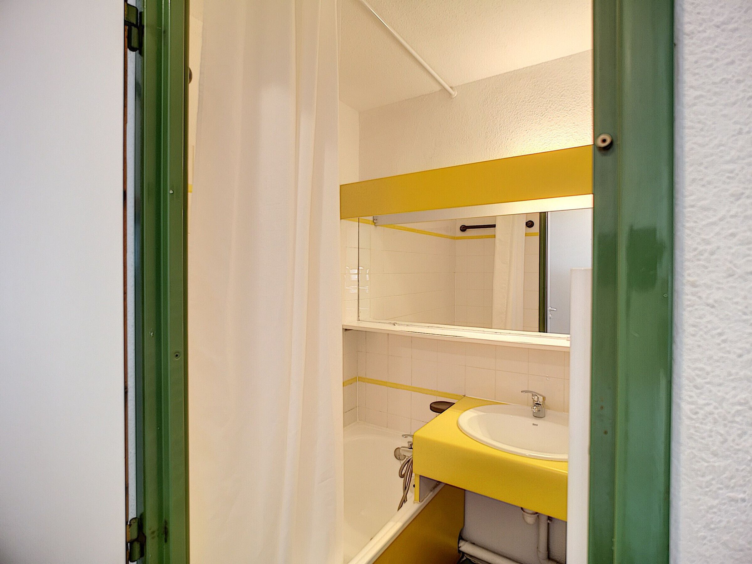 Un baño con un lavamanos amarillo, azulejos blancos y un marco de puerta verde.