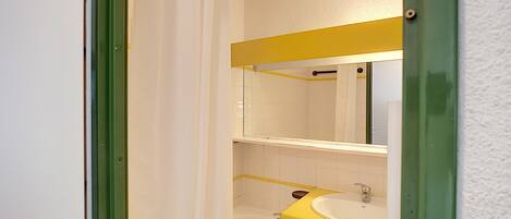Un baño con un lavamanos amarillo, azulejos blancos y un marco de puerta verde.