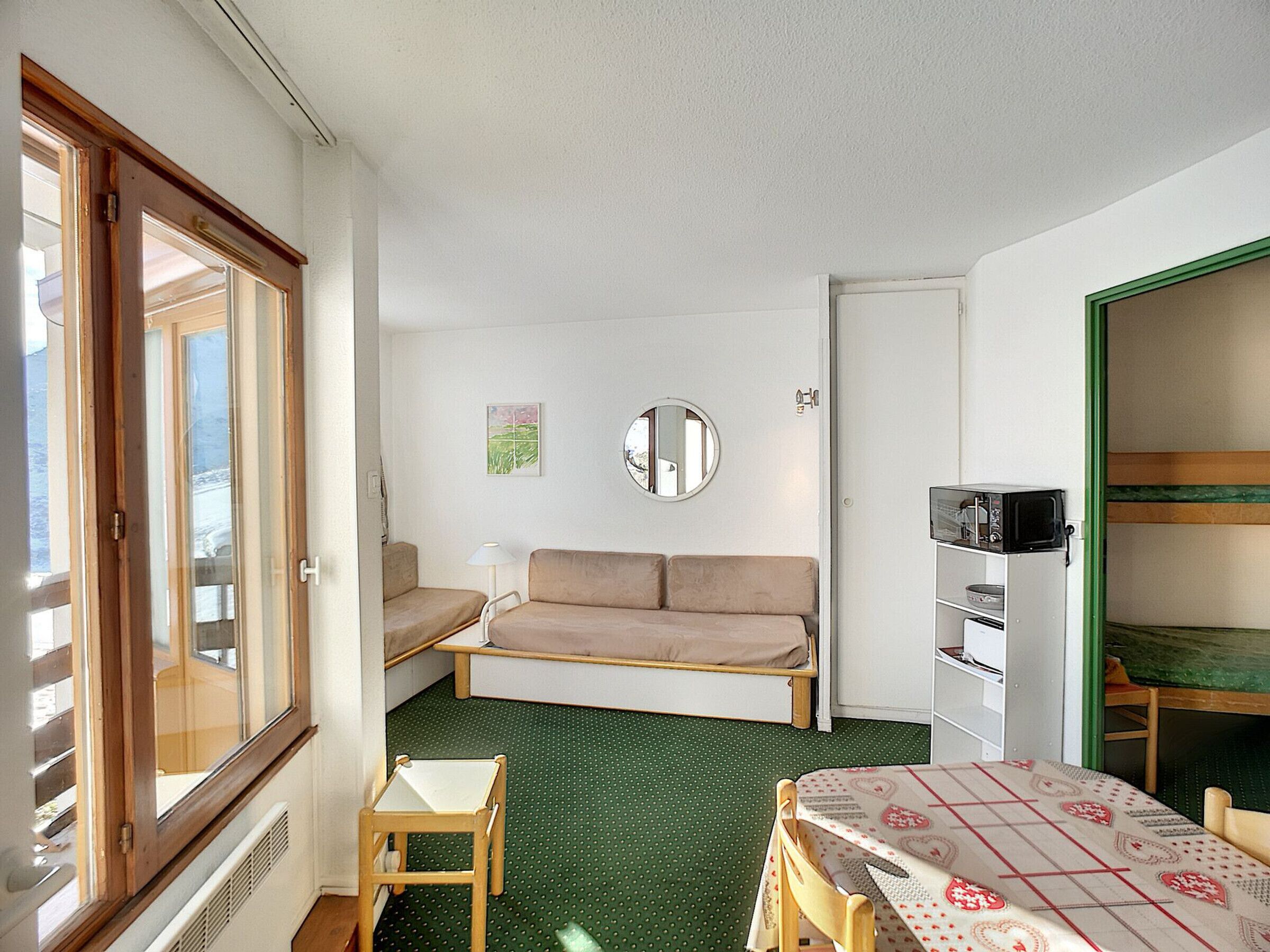 A small, compact room with a sofa, a small table, a television, and a microwave.